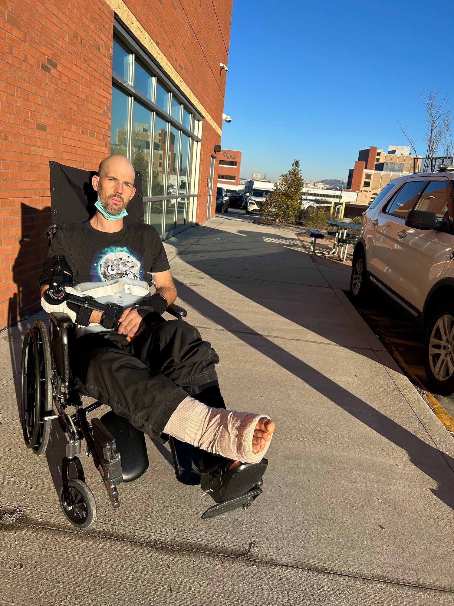 A man in a wheelchair with a cast on his foot is sitting on the sidewalk.