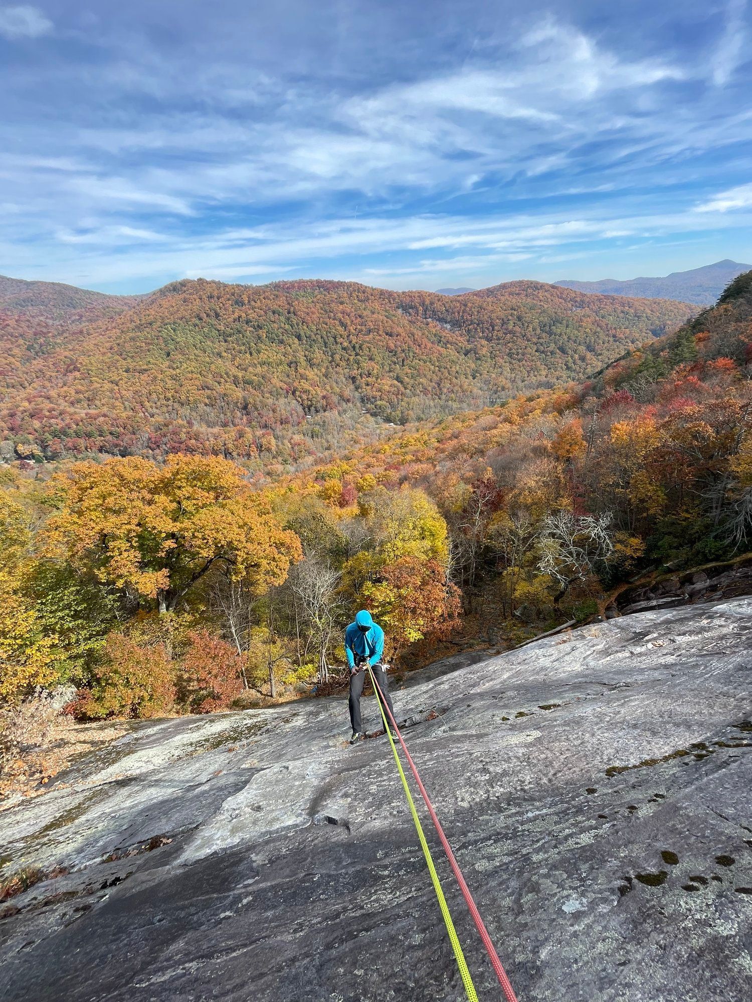 A person is climbing up a rocky cliff with a rope.