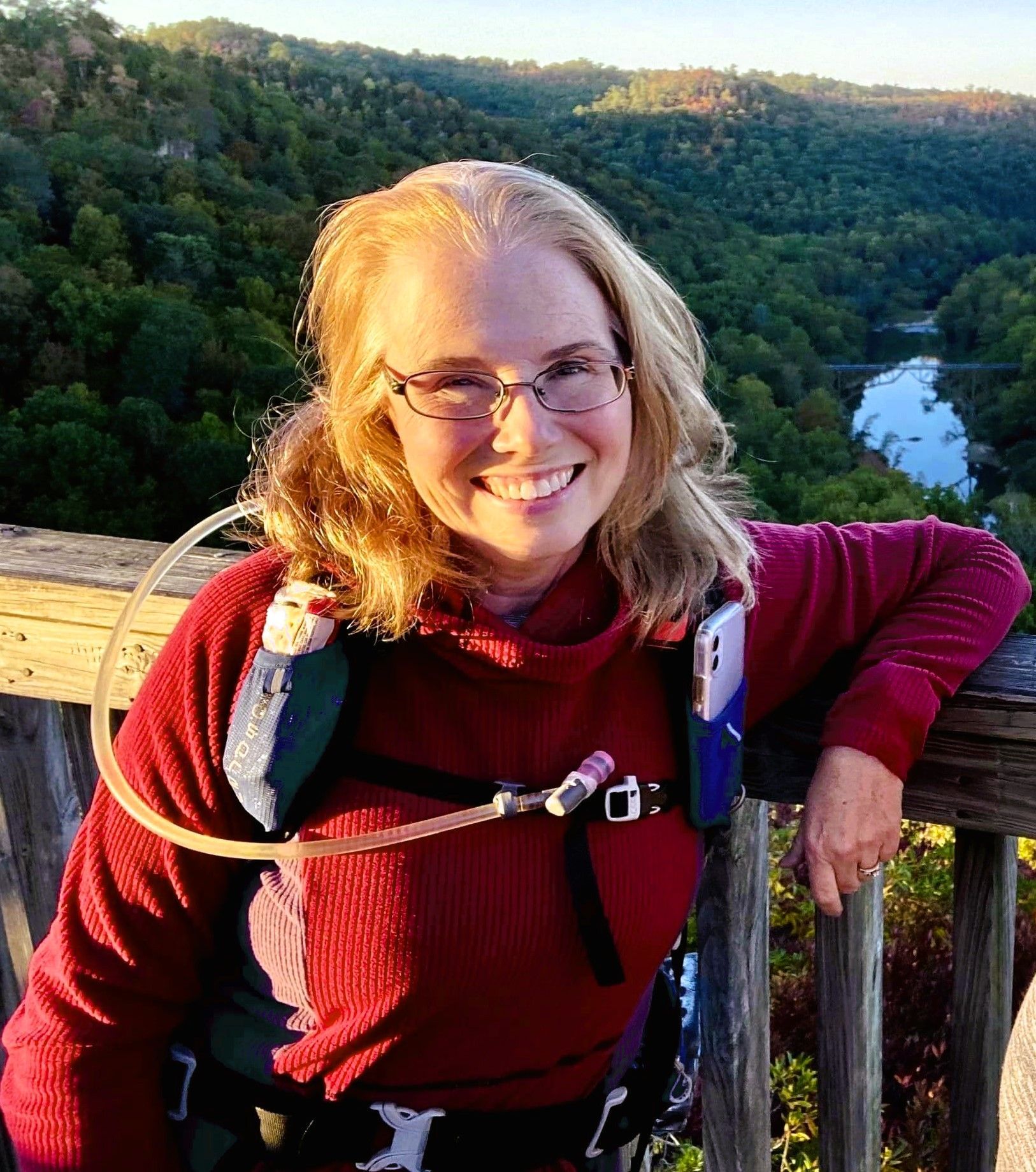 A woman in a red sweater is leaning on a railing and smiling