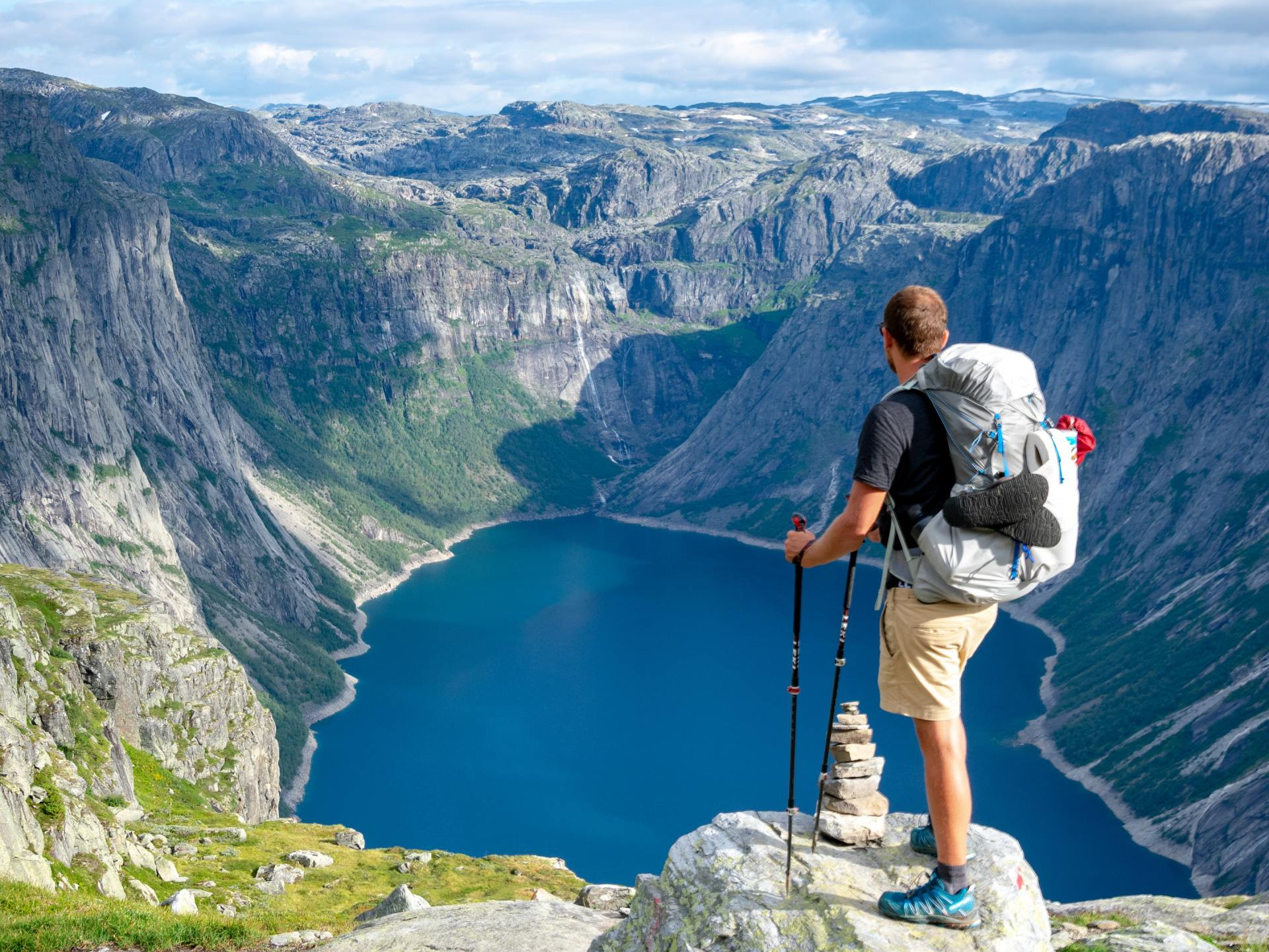 A man with a backpack is standing on top of a mountain overlooking a lake.