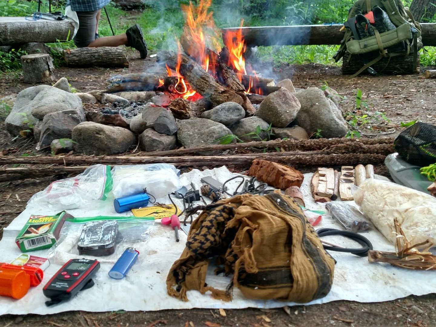 A person is kneeling in front of a campfire.