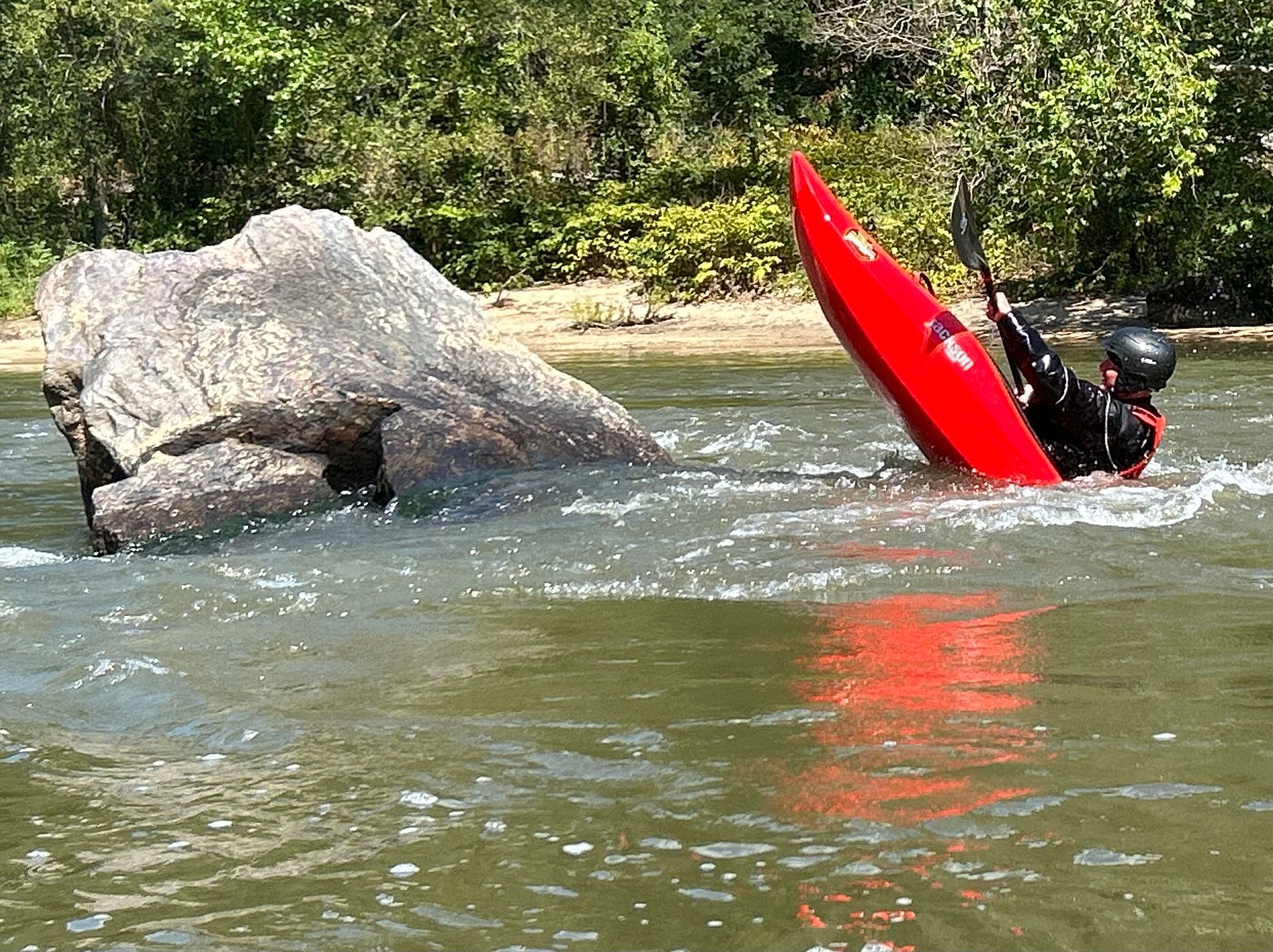 A person in a red kayak is paddling down a river.