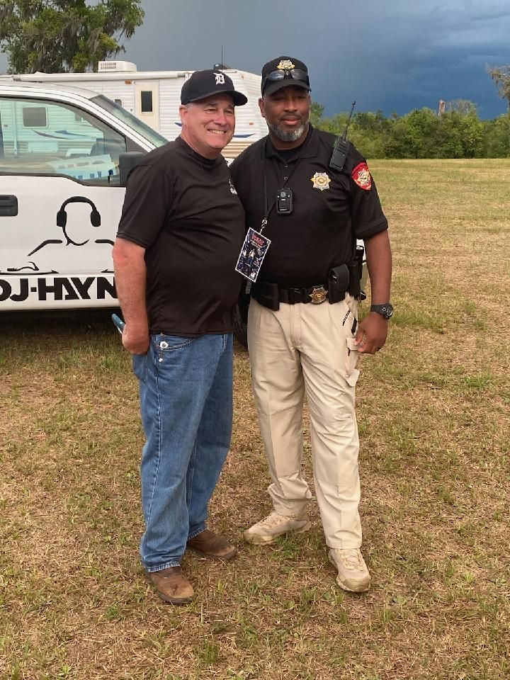 Two men posing outdoors beside a white helicopter on a grassy field.