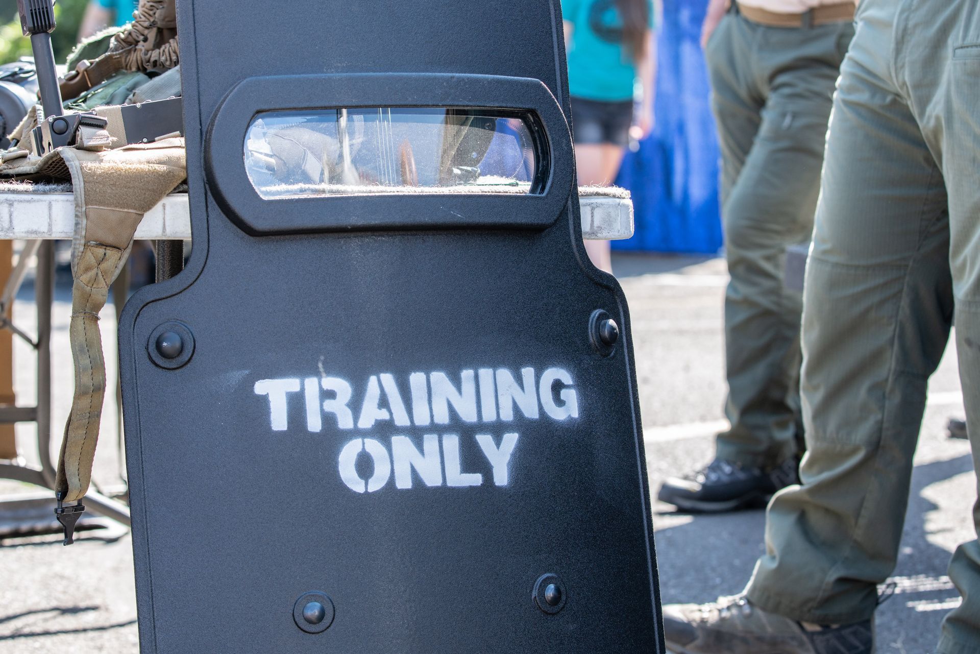 Black training shield marked “TRAINING ONLY” outdoors with people and equipment in the background