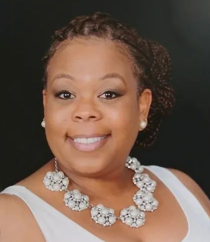 Smiling person in a white dress with pearl jewelry against a dark background