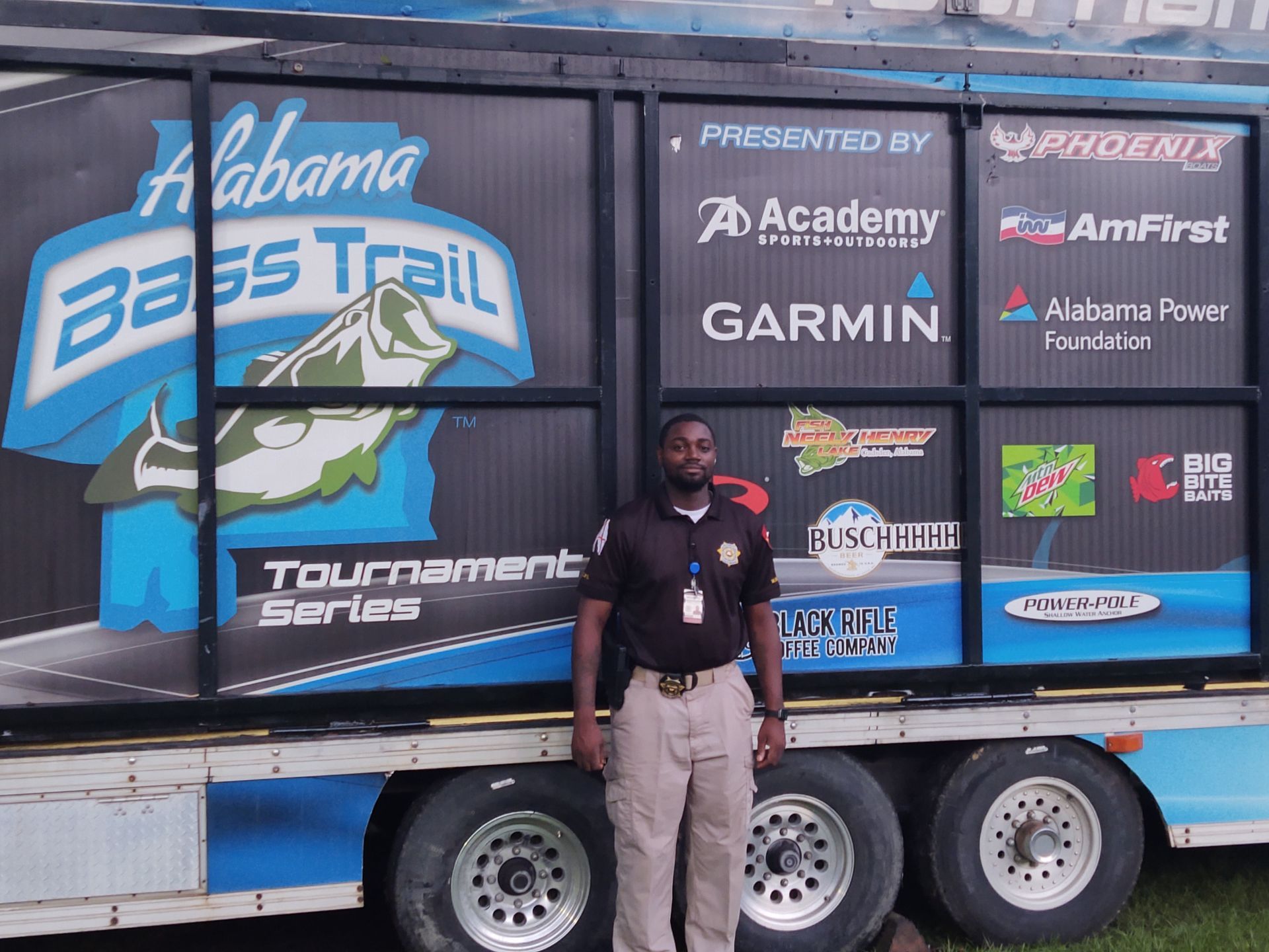 Person standing in front of a large black and white race trailer with sponsor logos outdoors