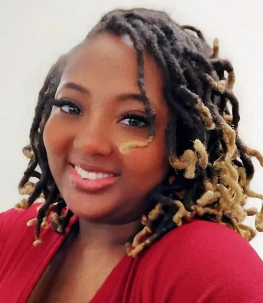 Smiling woman with shoulder-length blond-tipped locs wearing a red top on a white background
