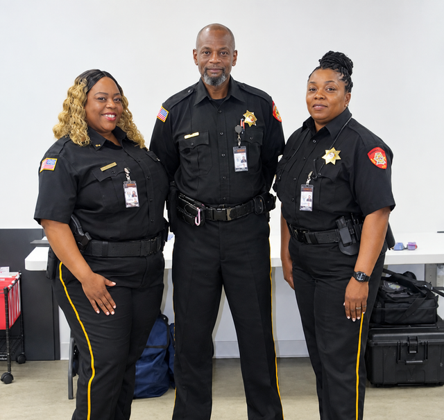 Three uniformed security officers posing indoors against a plain wall.