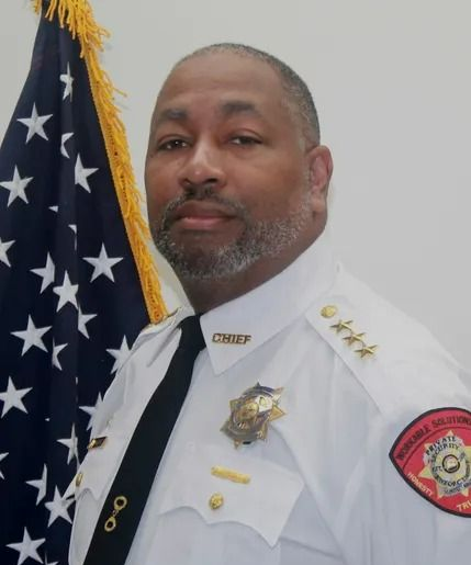 Uniformed officer standing beside an American flag, wearing a white shirt with insignia.