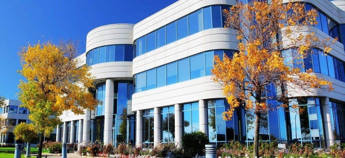 Modern blue-glass office building with curved facade and autumn trees in front