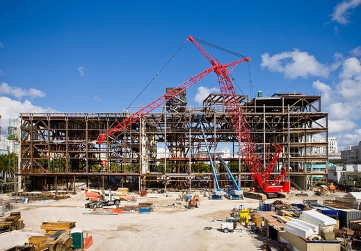 Construction site with steel frame building and red cranes under a blue sky