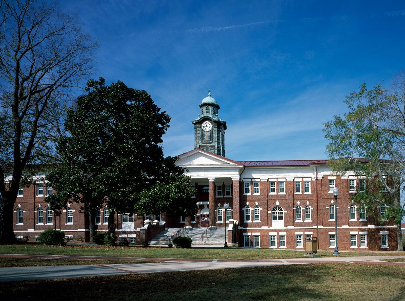 Red-brick campus building with white columns and a clock tower under a blue sky