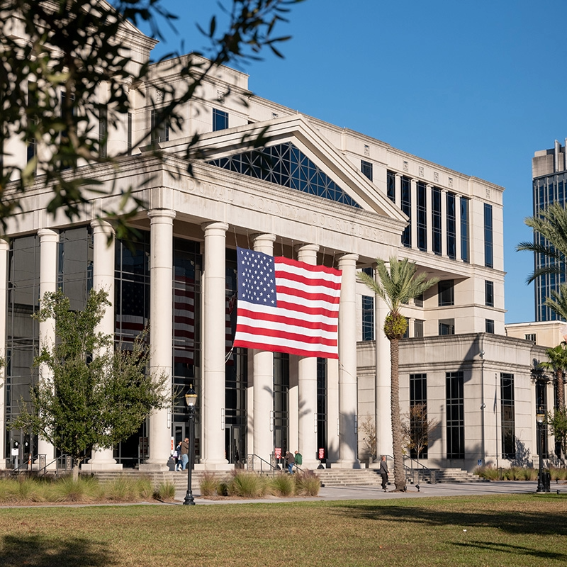 U.S. Capitol-style building with columns and a large American flag on a sunny day