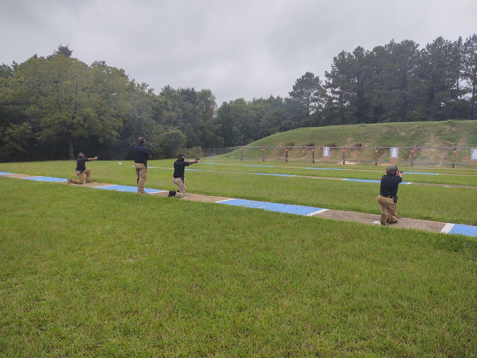 People on a grassy field beside a blue track under a cloudy sky