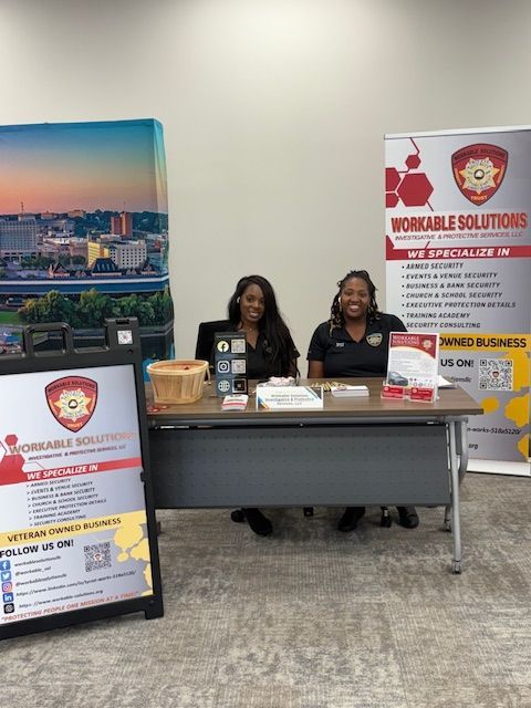 Two women seated at a booth with Workable Solutions signage and brochures in a conference hall