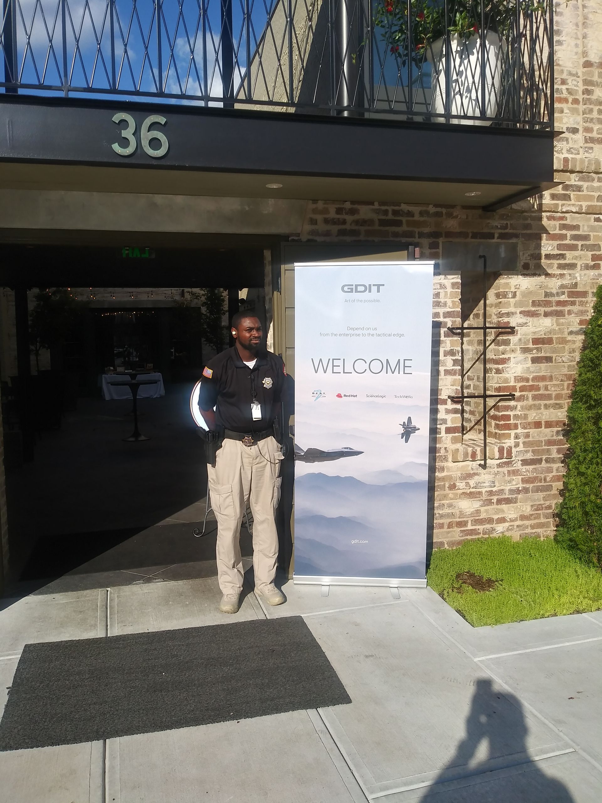 Security guard standing outside building entrance beside a welcome sign, under the number 36.