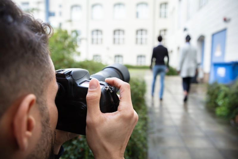 Photographer aiming a camera at two blurred people walking on a wet city street