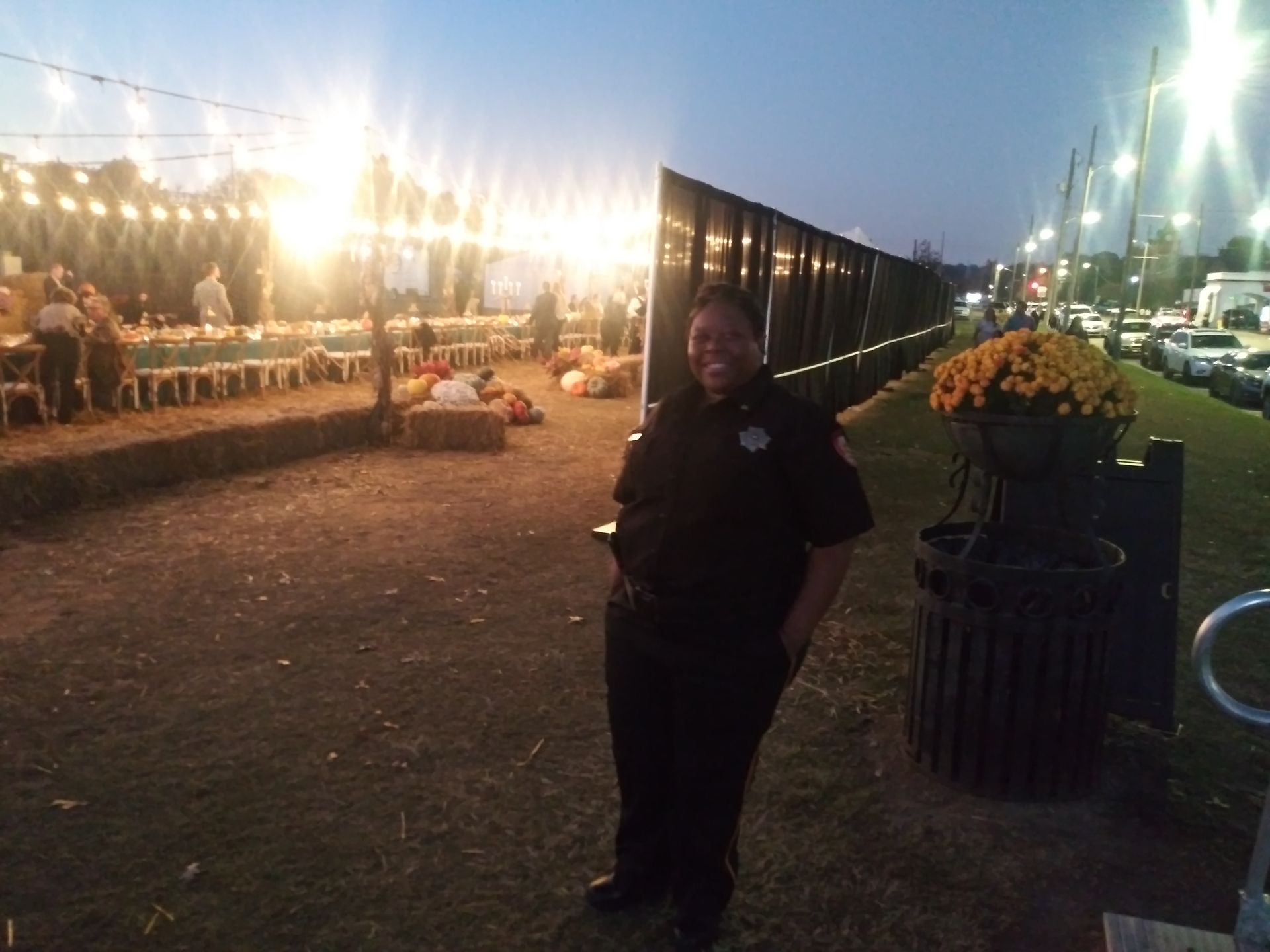 Person standing at an outdoor evening event beside a lit walkway and flower planters