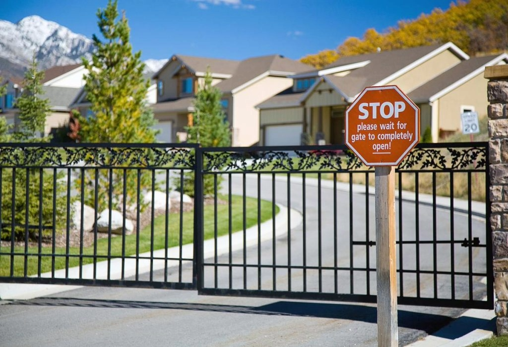 Gated suburban apartment entrance with a stop sign and black metal fence, snow-capped mountains in background