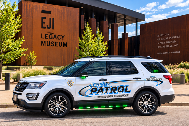 White patrol SUV parked outside the EJI Legacy Museum entrance with trees and modern brick buildings.