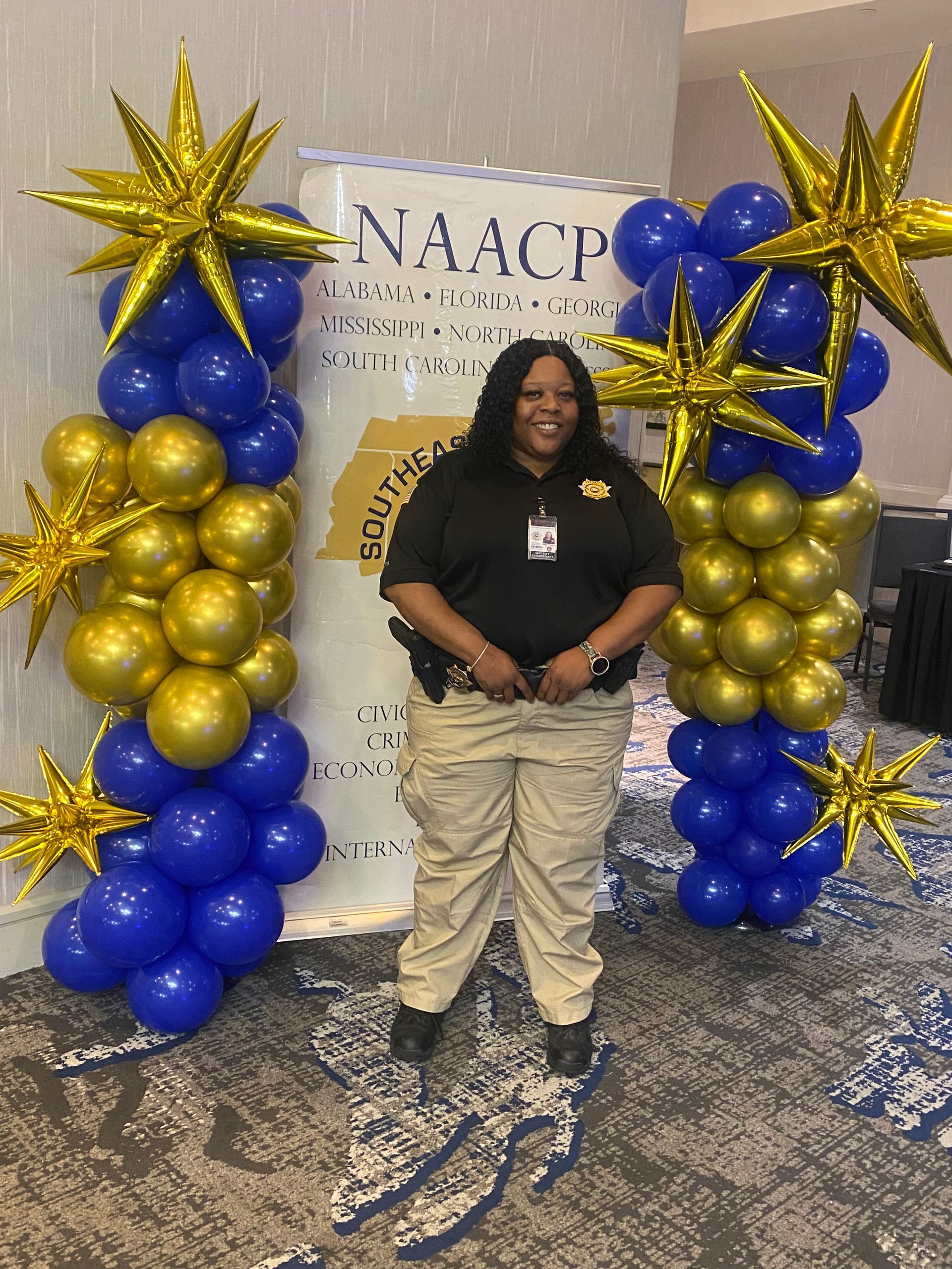 Person standing between gold and blue balloon columns at an NAACP event banner.