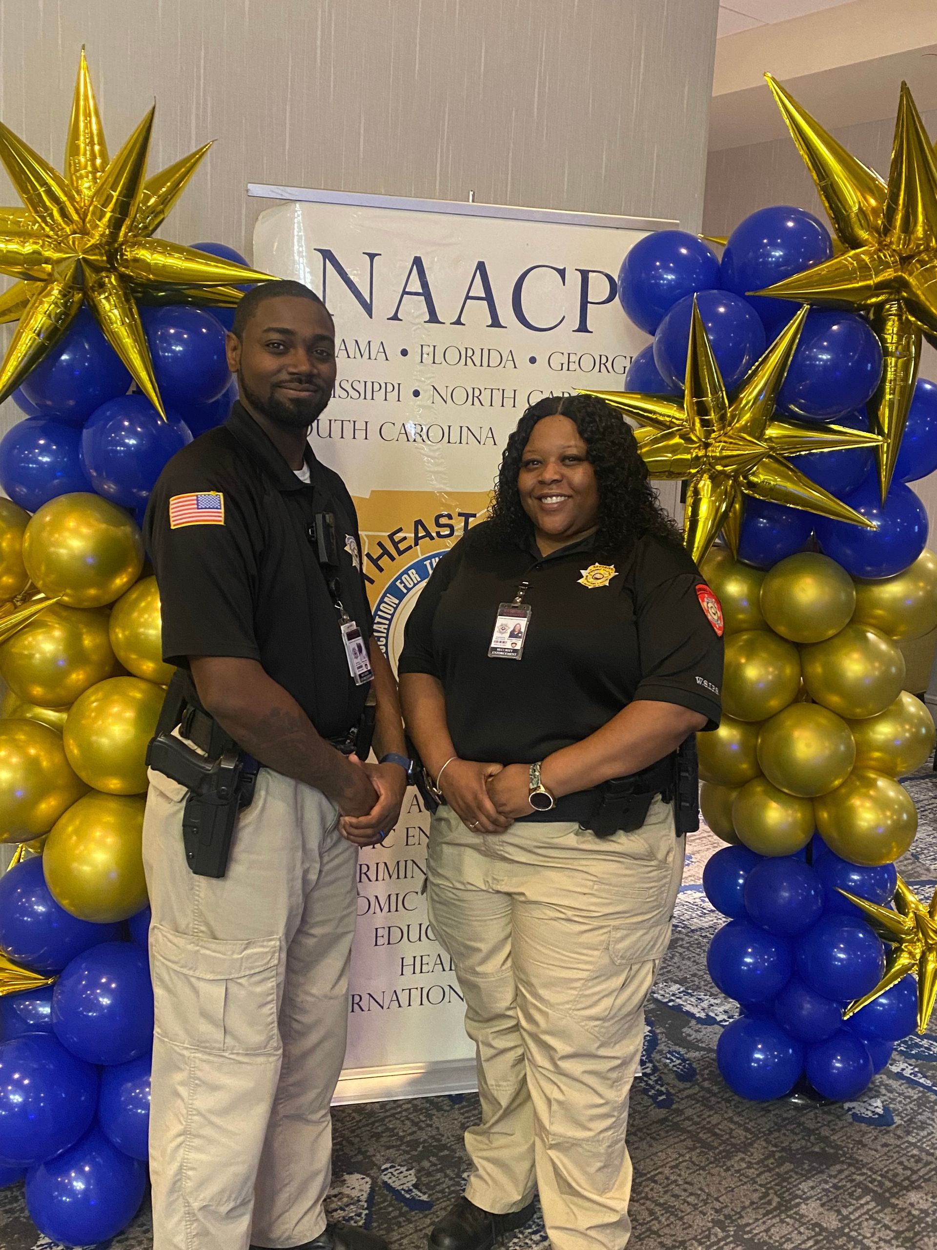 Two people pose at a NAACP event with blue, gold, and white balloon decorations.