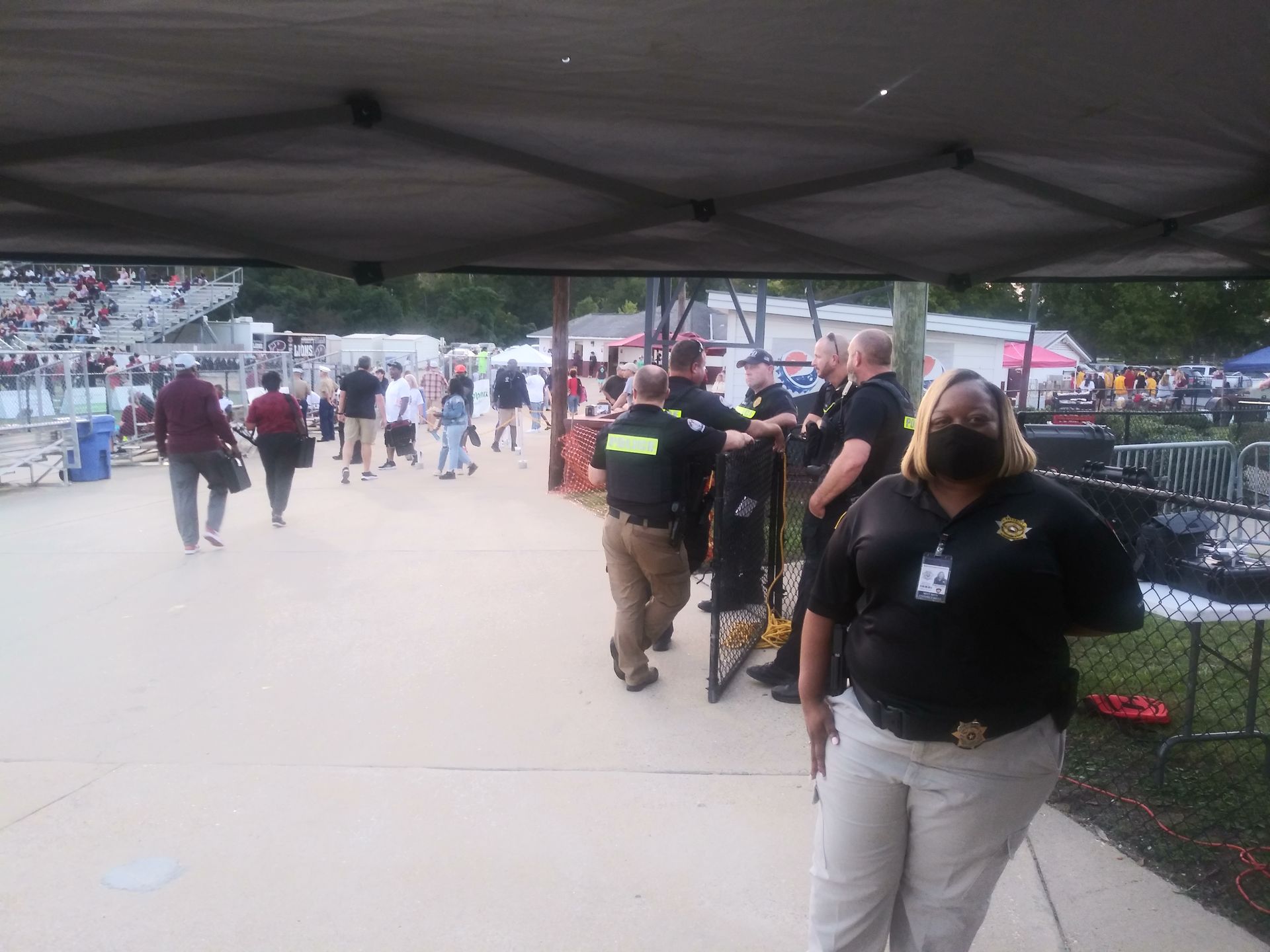 People walking through an outdoor event under a canopy tent, with staff in black shirts nearby.