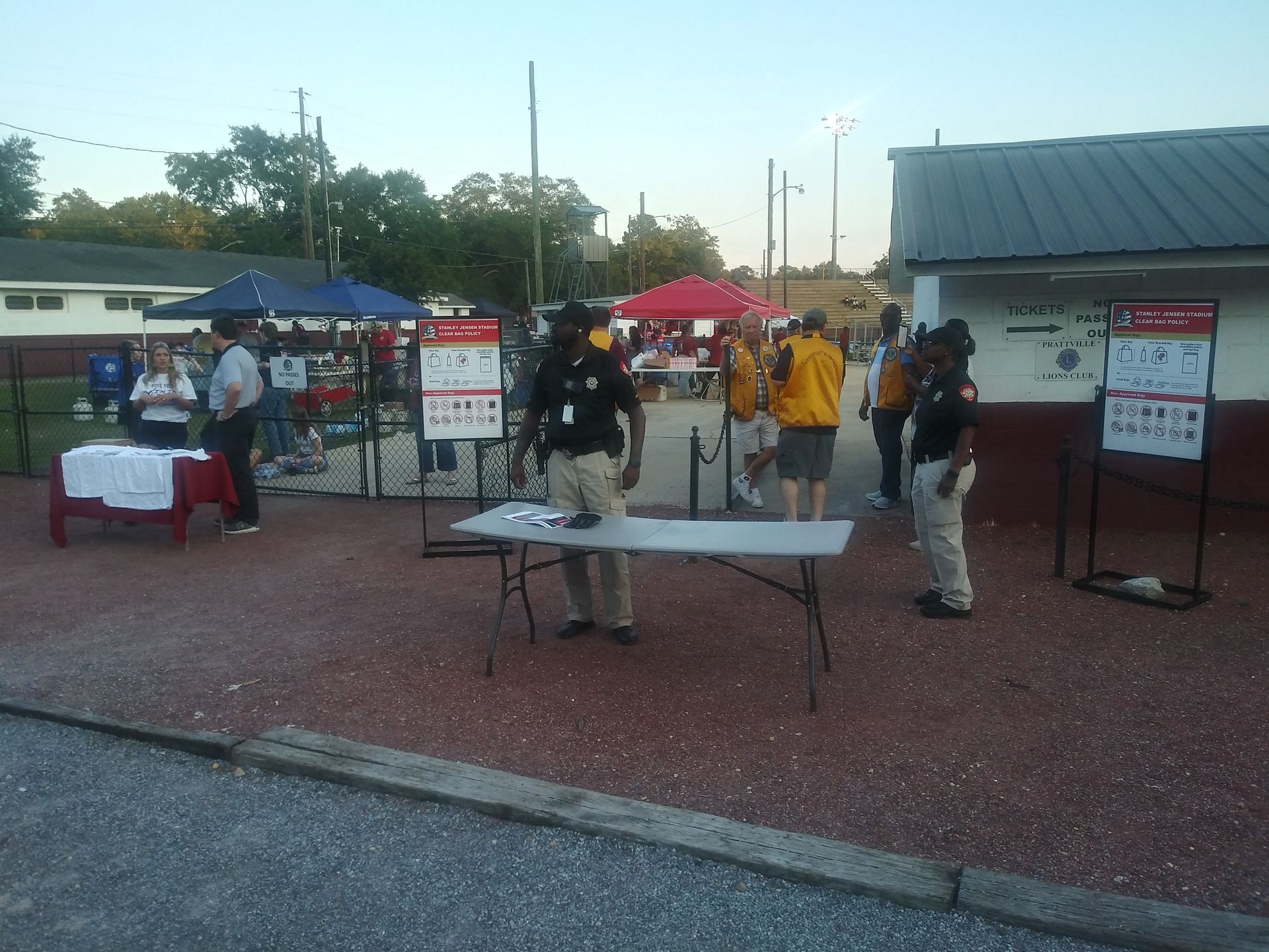 Outdoor community event with tables, tents, and people gathered in a gravel lot at dusk