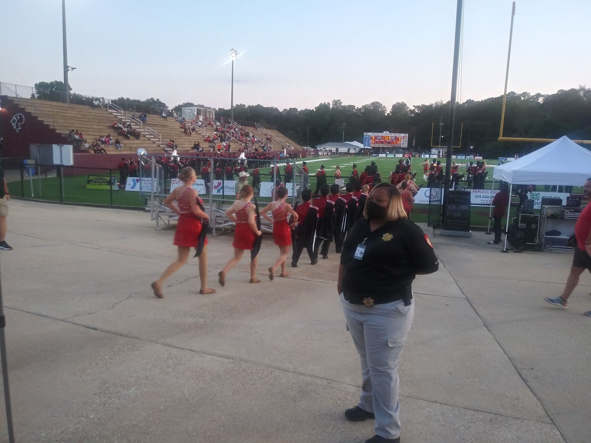 Marching band and dancers perform on a stadium field, with a photographer in the foreground.