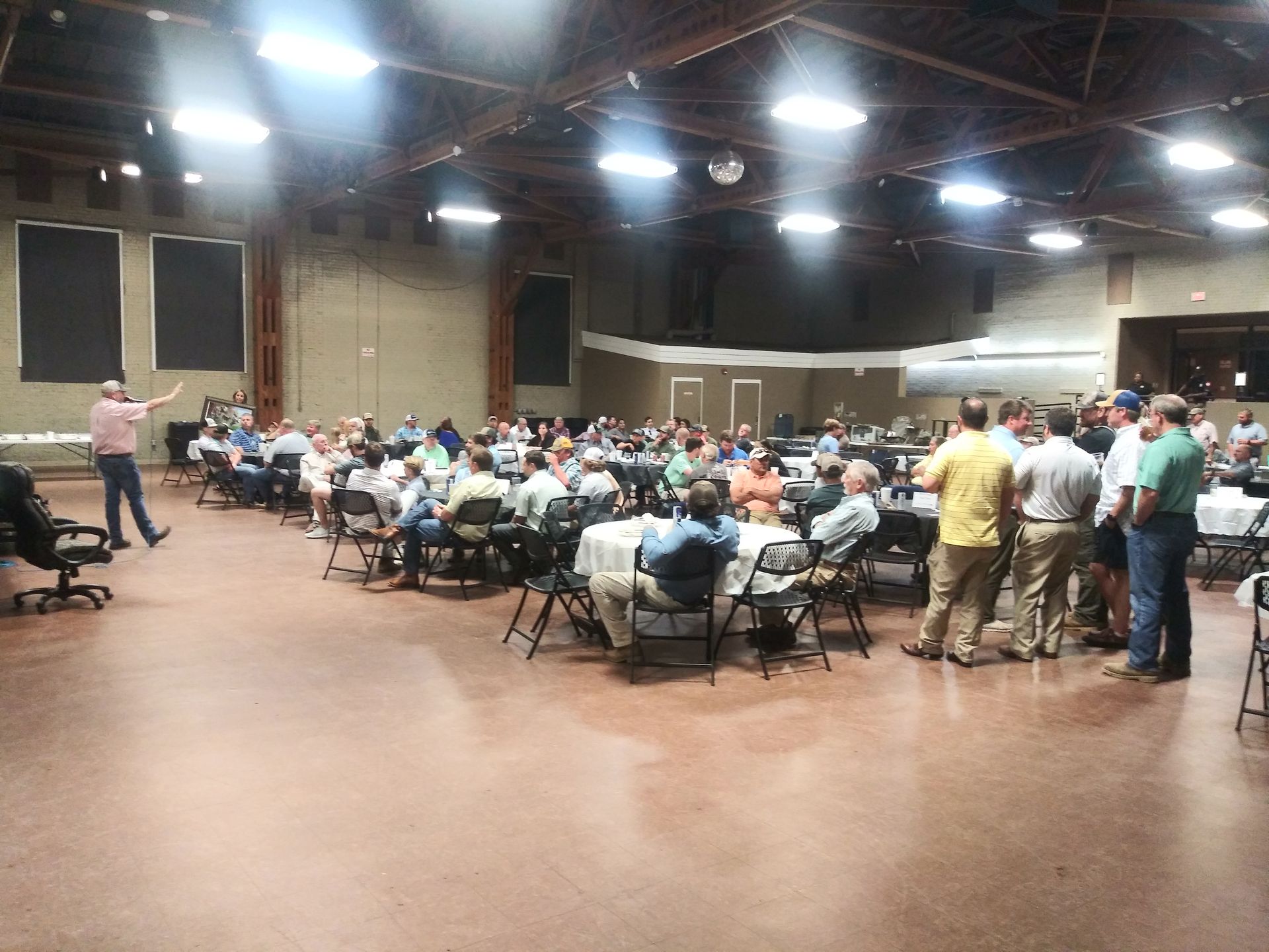 Large meeting hall with a seated audience and a presenter speaking at the front.