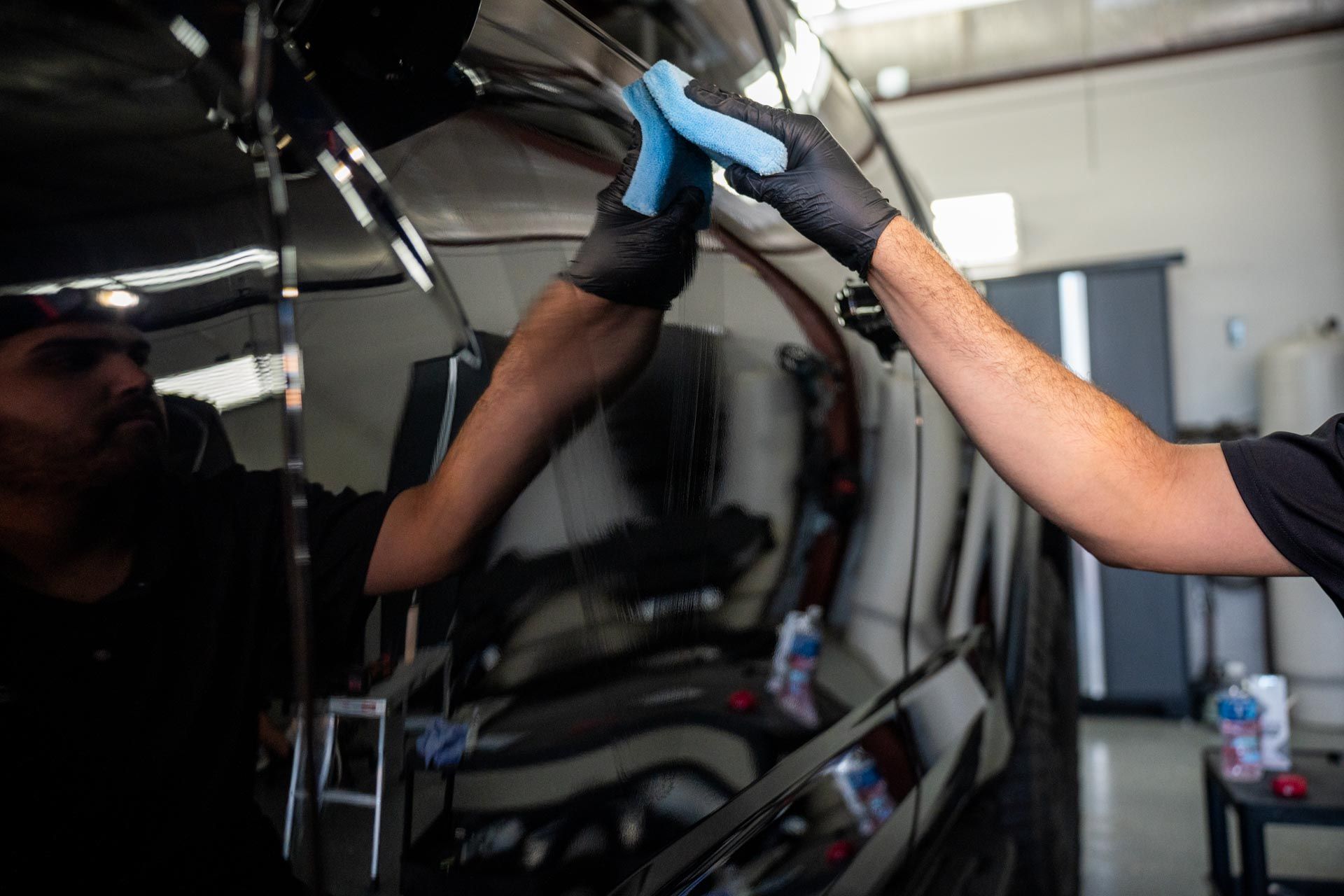 Gloved hands polishing a black car’s side panel in a workshop