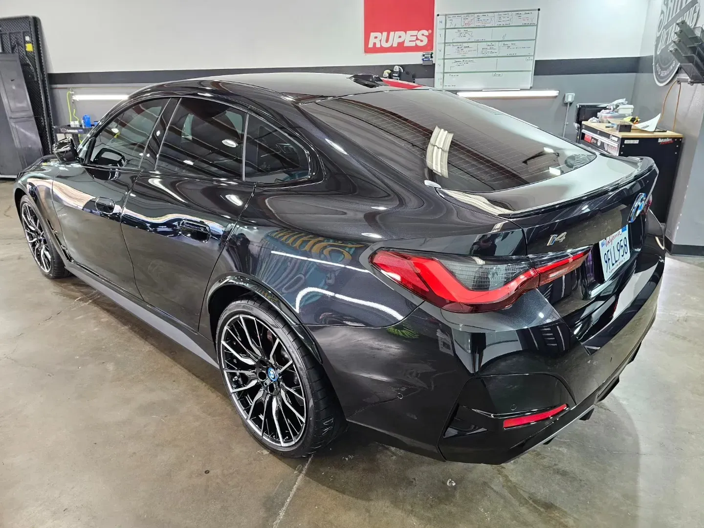 Black sports sedan in an auto detailing shop, rear three-quarter view, with glossy paint and custom wheels