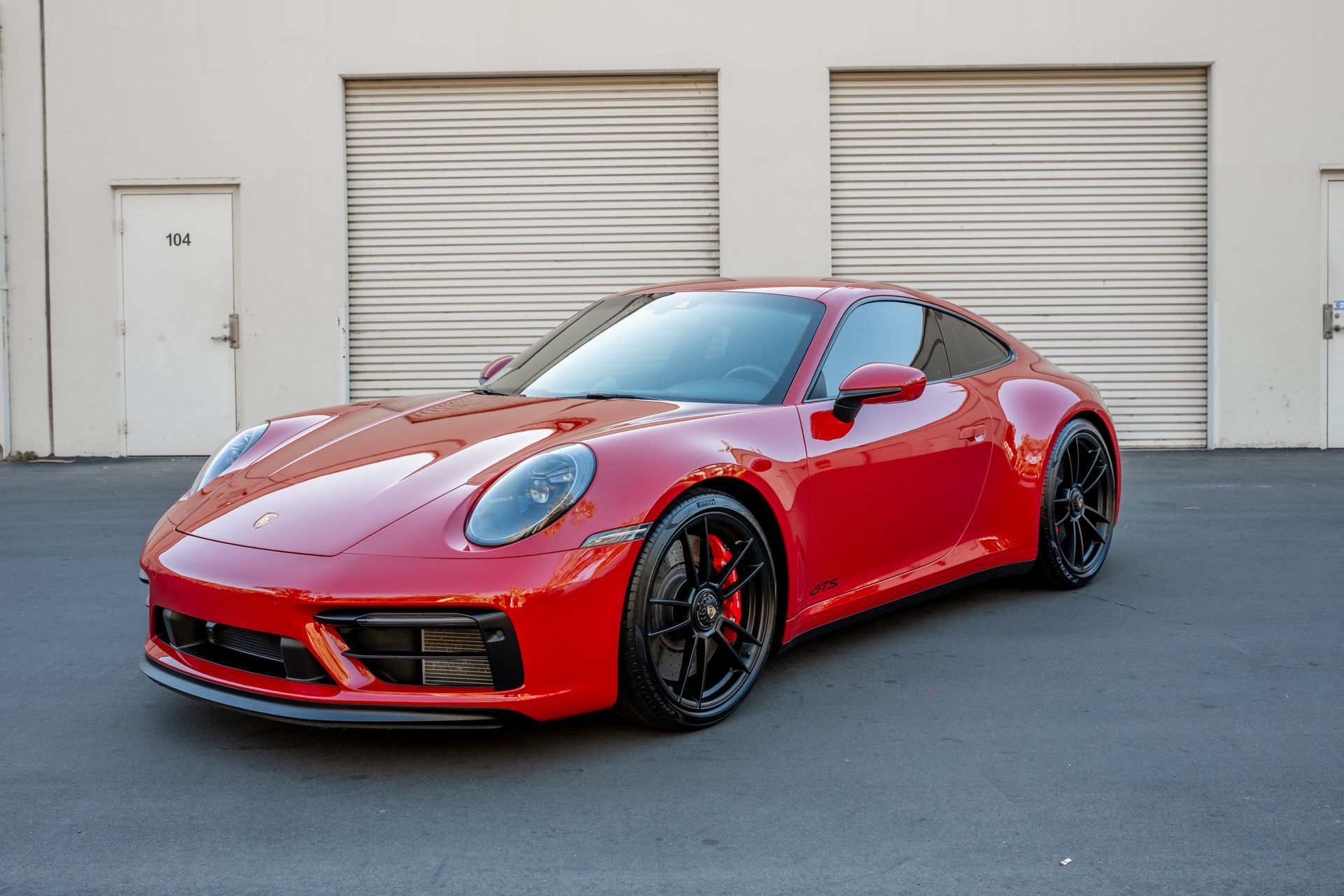 Red Porsche 911 coupe parked in front of a building with closed garage doors.