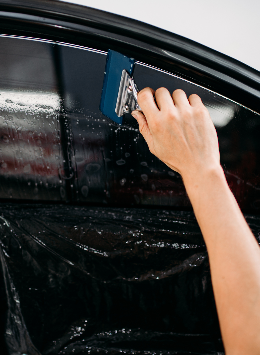 A person is applying tinted window film to a car window.