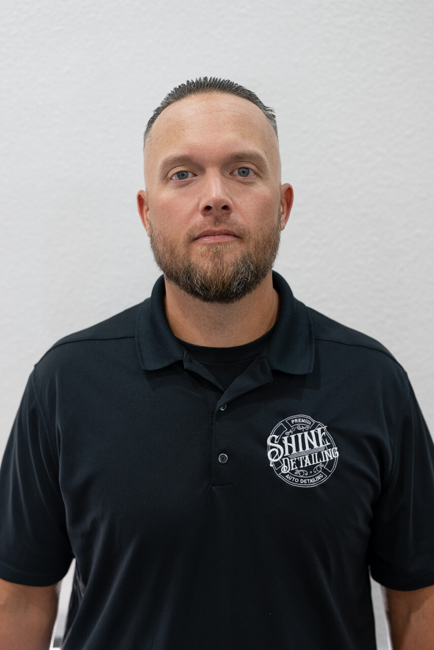 Man in black polo shirt standing against a plain white wall