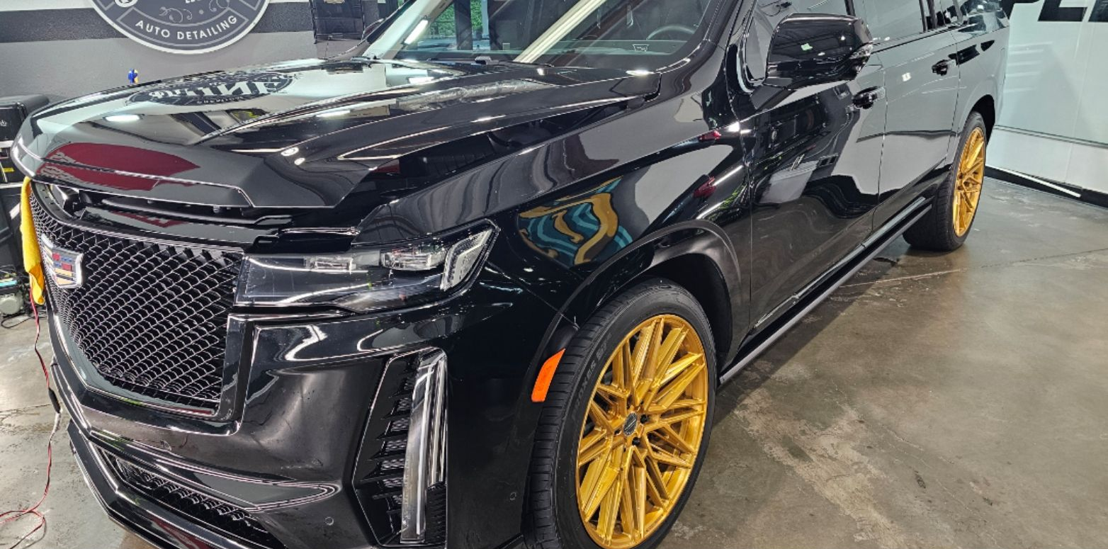 Black Cadillac SUV with gold wheels in an indoor showroom