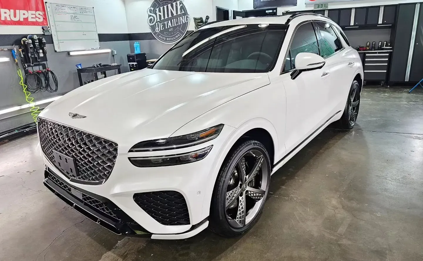 White Genesis GV70 SUV parked indoors with a glossy finish, featuring a dark grille and wheels.