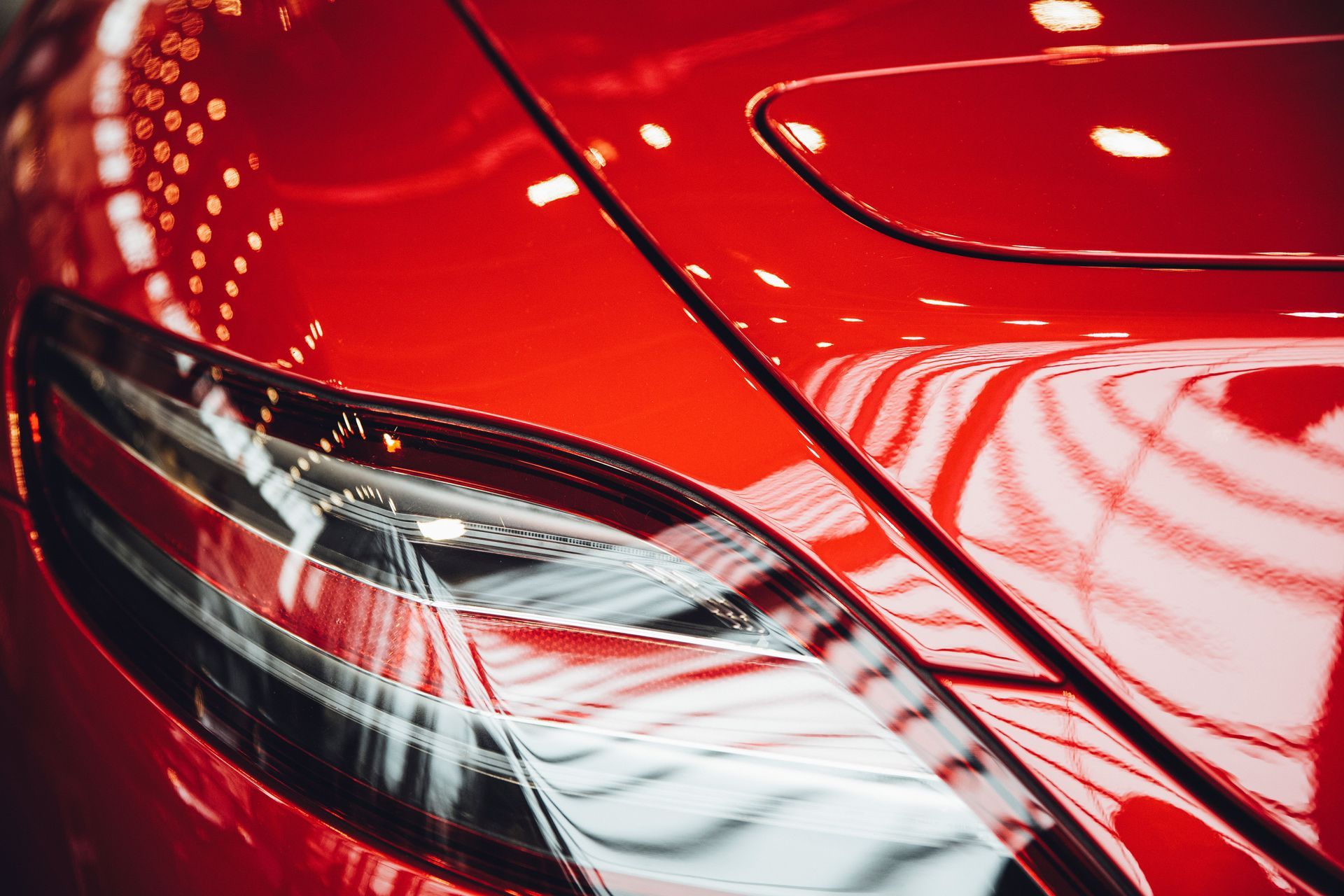 Close-up of a glossy red car headlight and front fender with reflections