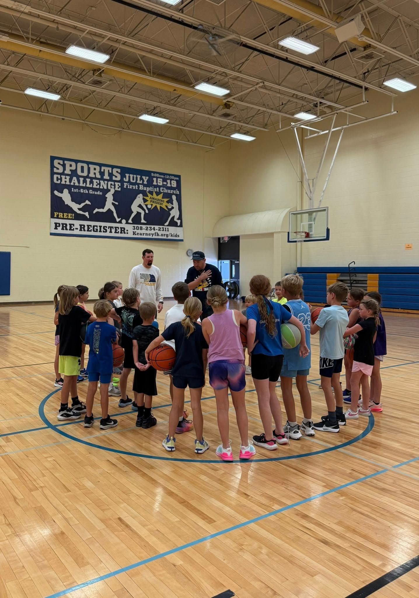 Children gathered in a gymnasium around a basketball hoop during a group activity