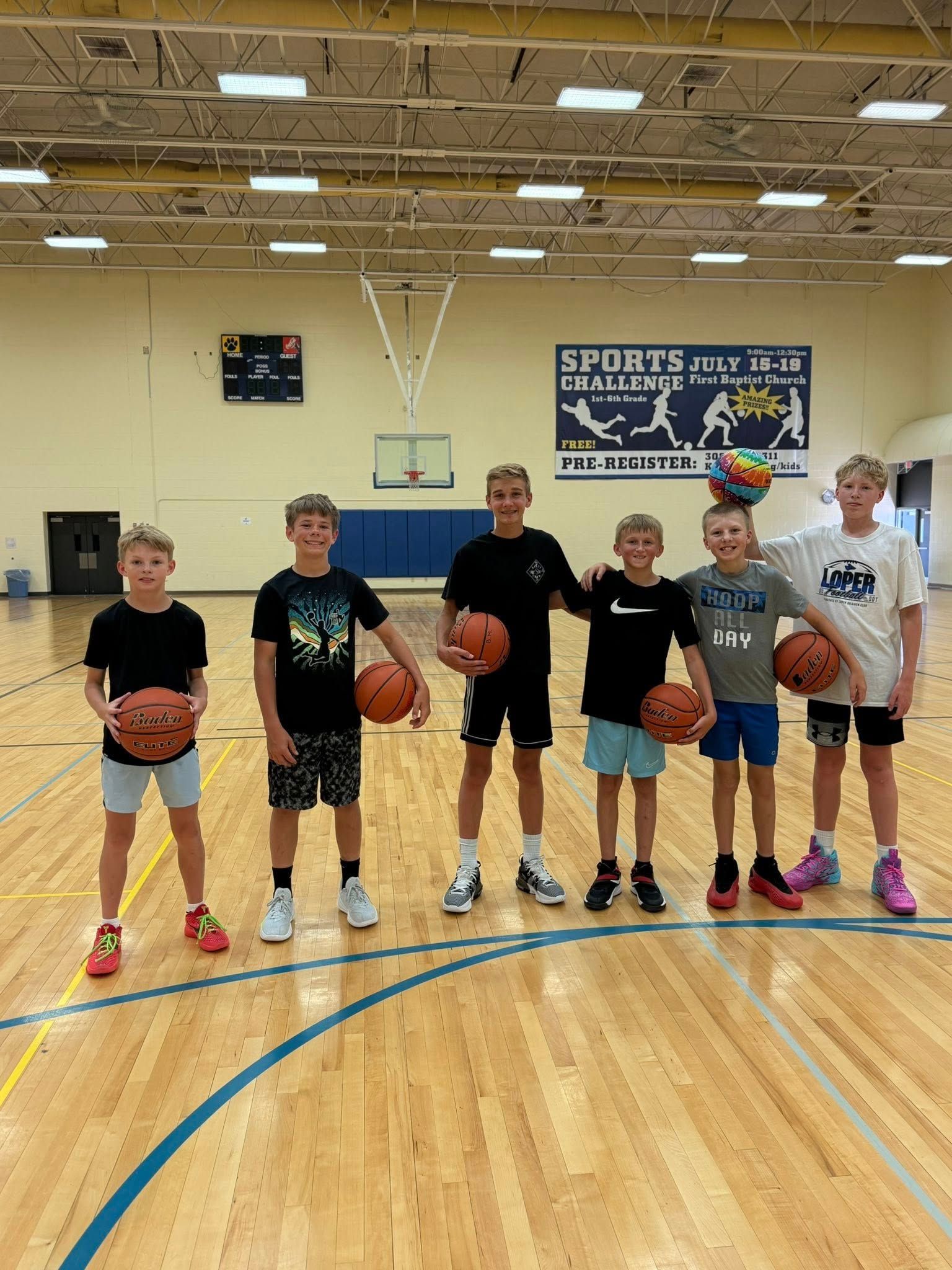 Six kids stand on a gym court holding basketballs during a team photo.