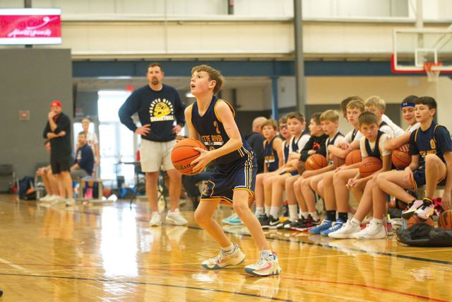 Youth basketball player dribbling on indoor court as teammates and coach watch from the sideline