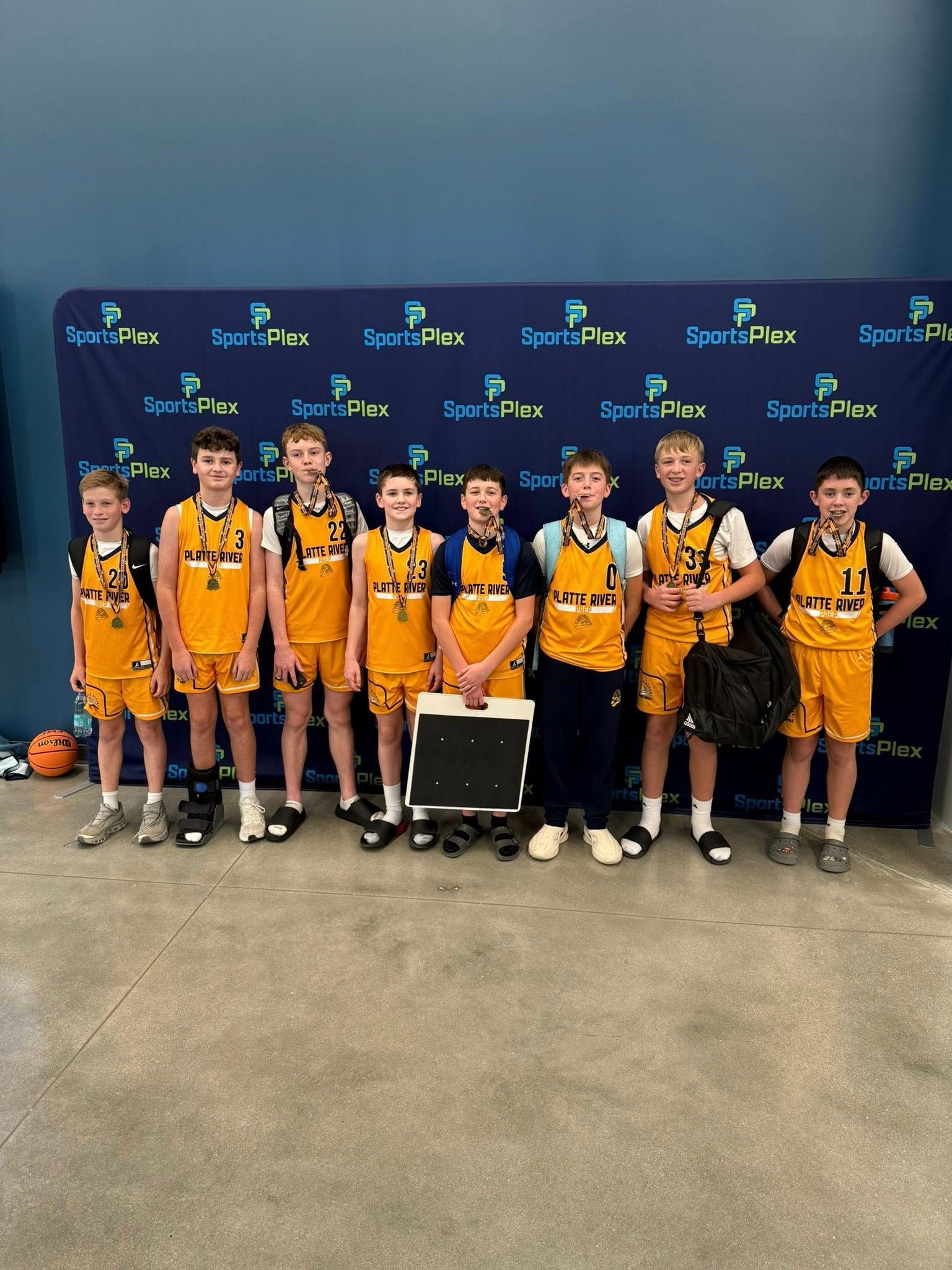 Youth basketball team in yellow uniforms posing in a gym before a blue backdrop