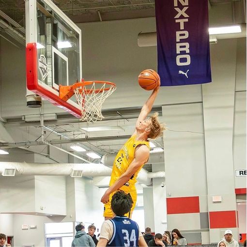 Basketball player in yellow jersey leaps for a layup over a defender in an indoor gym.