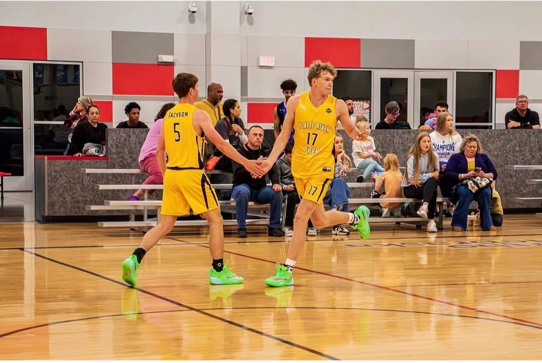 Youth basketball game in a gym, with a player dribbling past a referee and spectators in the background