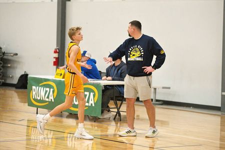 Basketball player in yellow and orange uniform talks with coach on court during a game