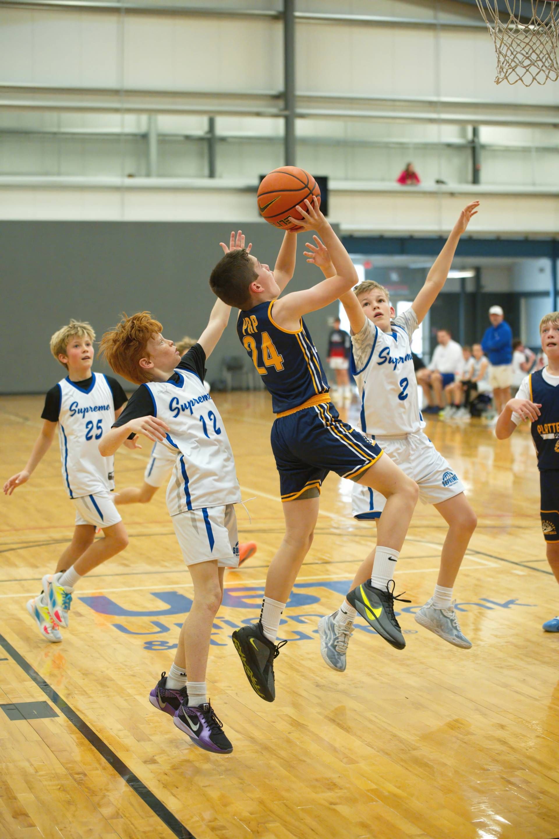 Basketball player in dark jersey jumps for a shot as defenders in white contest under the hoop