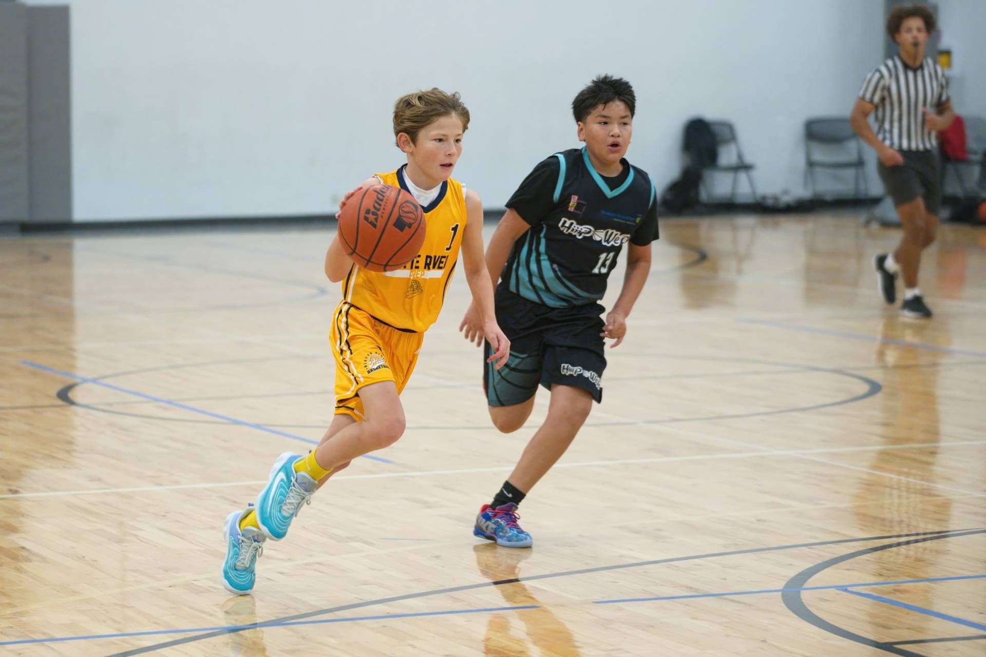 Two youth basketball players sprint down the court, one in yellow and one in black, during a game.