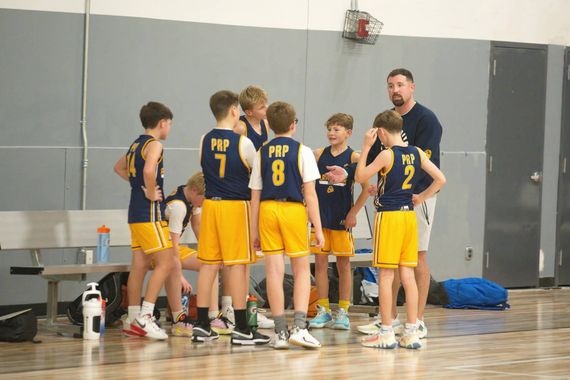 Basketball team huddling with coach in a gym during a timeout.