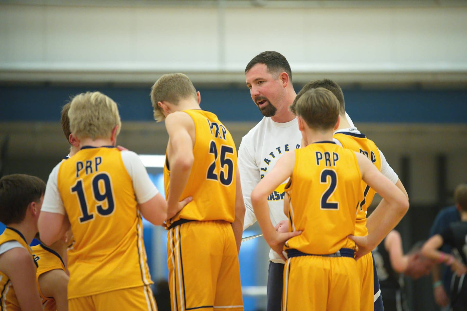 Youth basketball coach huddles with three players in yellow uniforms during a game timeout