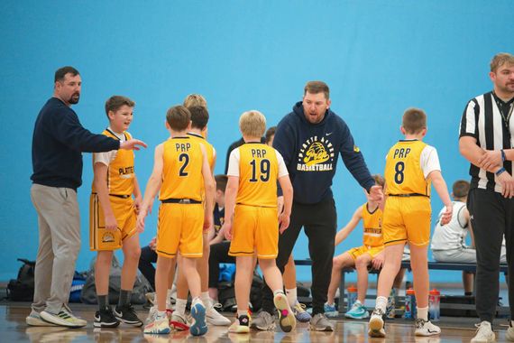 Youth basketball team huddles with coaches on the sideline during a timeout